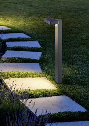 marble path of square tiles illuminated by a lantern glowing with a warm light in a backyard garden with a flower bed and a lawn copy space.